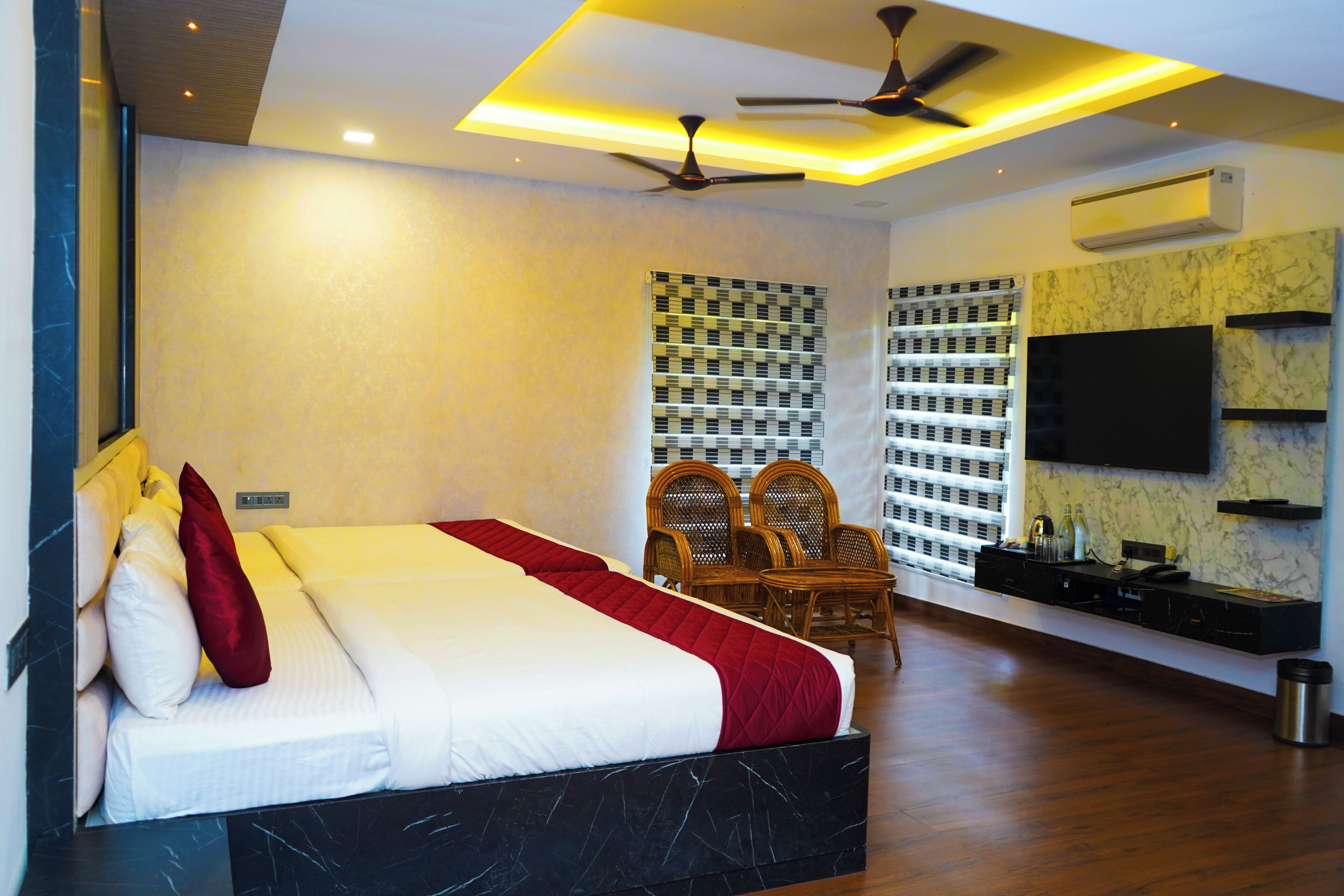 A modern hotel room with a large bed, a ceiling fan, a TV, and a minibar.