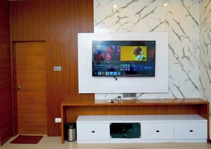A modern living room with a flat-screen TV mounted on a wooden wall, a white entertainment unit below, and a marble-patterned wall. - Winners Hill Resort Walayar by Arcadia (Coimbatore)