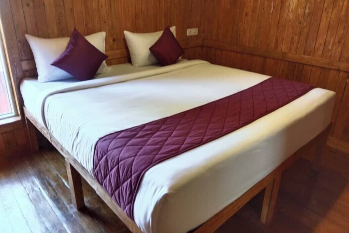 A wooden-framed bed with white and purple bedding, a wooden floor, and a wooden wall.