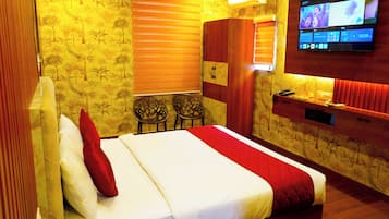 Habitación de hotel con cama, televisión montada en la pared, escritorio con teléfono y una silla.