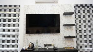 A modern room with a flat-screen TV mounted on a marble wall, air conditioning above, and a coffee station with a kettle and cups. - WINNERS HILL RESORTS (Coimbatore)