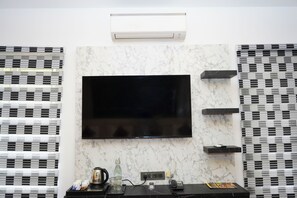 A modern room with a flat-screen TV mounted on a marble wall, air conditioning above, and a coffee station with a kettle and cups. - WINNERS HILL RESORTS (Coimbatore)