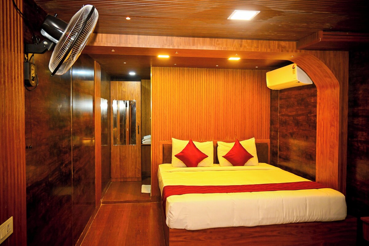 Una camera d'albergo con soffitto in legno, un letto con biancheria da letto bianca e rossa, una ventola da terra e un condizionatore d'aria a parete.