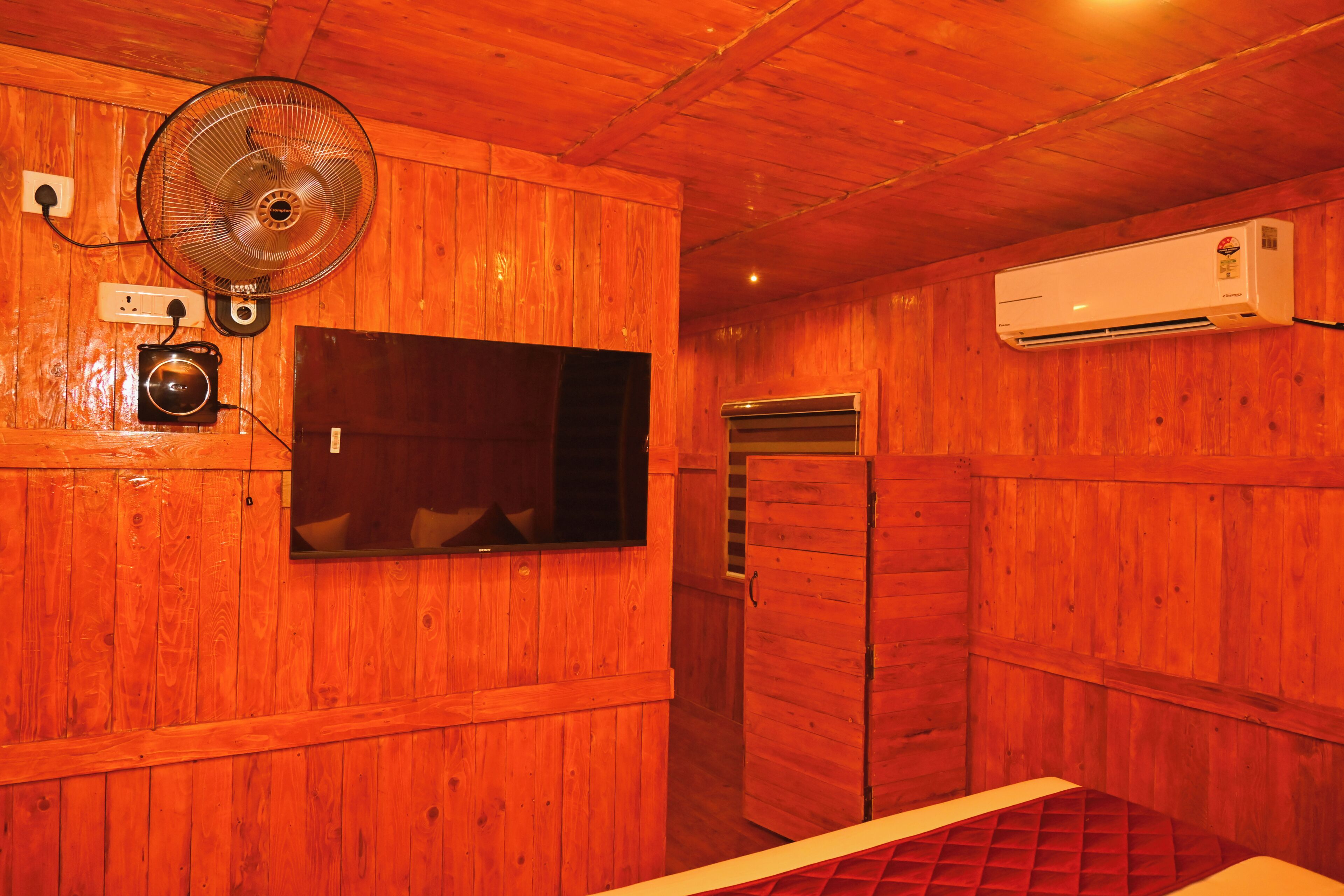 Quarto de madeira com ventoinha, televisão e aparelho de ar condicionado.