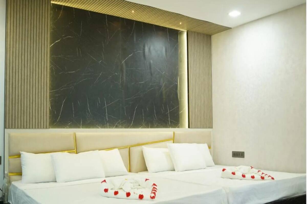 A hotel room with a large bed, a marble headboard, and a large window with vertical blinds.