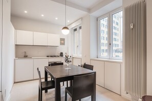 Una cocina moderna con armarios blancos, una mesa de comedor con sillas y una ventana con vista a edificios.