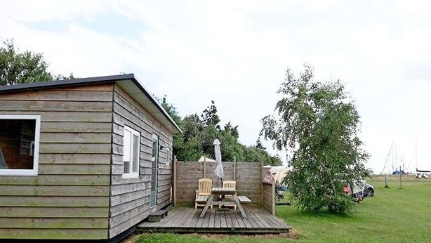 En stuga av trä med en veranda, två stolar och ett bord.