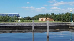 Ett lugnt vattenområde med en brygga, en liten byggnad och solpaneler i bakgrunden.