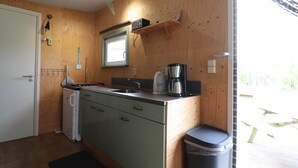 Ett litet, praktiskt kök med träväggar, en diskho, en kaffebryggare och en papperskorg.