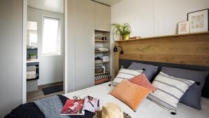 Un dormitorio con cama, mesitas de noche, cabecera de madera y estanterías empotradas con libros y objetos decorativos.