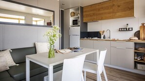 Una cocina moderna con armarios blancos, una encimera de madera y un microondas integrado. Hay una zona de comedor con una mesa y sillas blancas, y un sofá con un jarrón de flores.