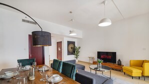 A modern living room with a dining area, a sofa, a yellow armchair, and a TV displaying 'NETFLIX'. - Elegant 1Br Apart With Beach Access In Dubai Creek (Dubai)