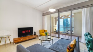 A modern living room with a grey sofa, a yellow armchair, a coffee table, and a TV displaying 'NETFLIX'. - Elegant 1Br Apart With Beach Access In Dubai Creek (Dubai)