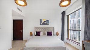 A modern bedroom with a large bed, a headboard, two bedside tables, a window with curtains, and a city view. - Elegant 1Br Apart With Beach Access In Dubai Creek (Dubai)