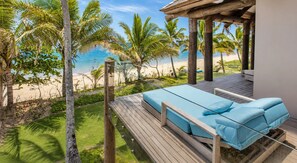Terraza de madera con una silla lounge azul acolchada que da a una playa.