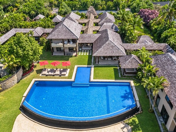 Un complejo turístico con varias construcciones, una piscina central y abundante vegetación.