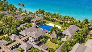 Un resort con varias construcciones tipo cabaña, una piscina central y vistas al océano.