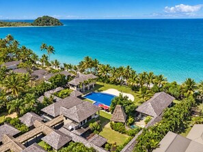 Un resort con varias construcciones tipo cabaña, una piscina central y vistas al océano.