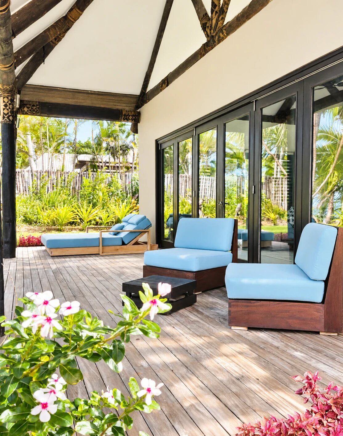 An outdoor seating area with a wooden deck, blue cushioned sofas, and a glass door leading to a garden.