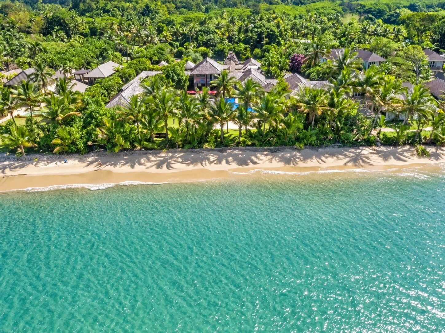 Un complexe hôtelier tropical situé en bord de mer, avec des plages, une eau turquoise cristalline et une végétation luxuriante.