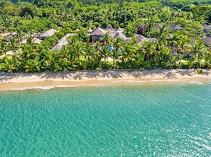 Un resort tropical con propiedades frente a la playa, aguas turquesas cristalinas y exuberante vegetación.