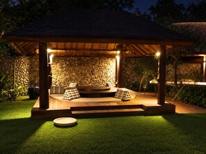A covered outdoor seating area with a stone wall backdrop, wooden steps, and a circular seating arrangement.