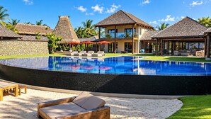 Un resort con piscina, sillas de descanso y construcciones de techo de paja.