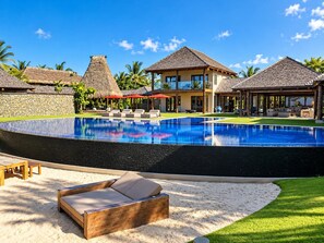 Un resort con piscina, sillas de descanso y construcciones de techo de paja.