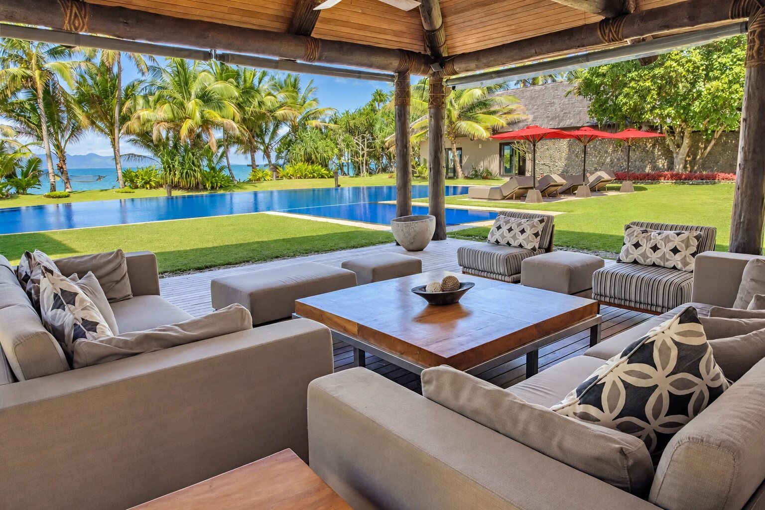 A covered outdoor seating area with a pool and tropical view.
