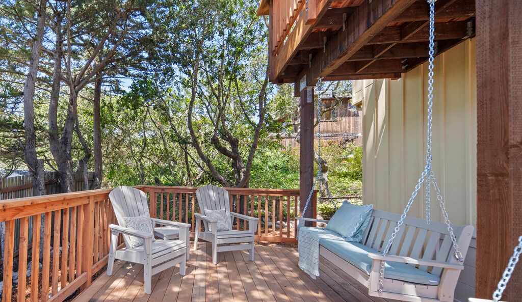 Una terraza de madera con dos sillas Adirondack y una silla colgante, rodeada de árboles.