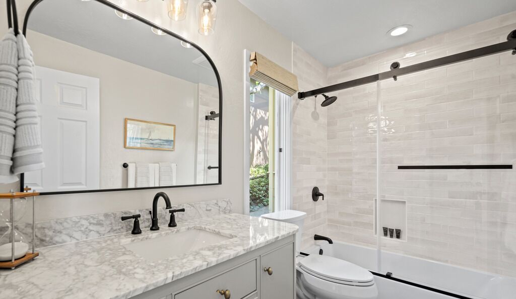 A modern bathroom with a marble sink, a large mirror, a glass shower enclosure, and a white toilet.