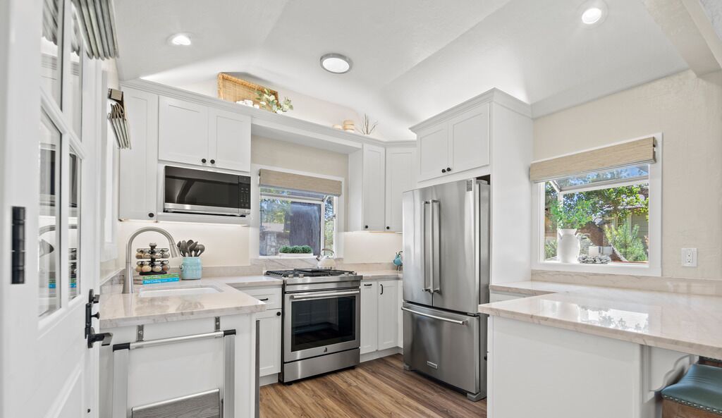 A modern kitchen with white cabinetry, stainless steel appliances, and a window providing a view of greenery outside.