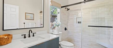 A modern bathroom with a large mirror, white sink, and a glass shower enclosure.