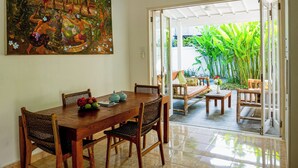 A dining area with a wooden table, wicker chairs, and a large painting on the wall. - Villa The White House Seminyak (Legian)
