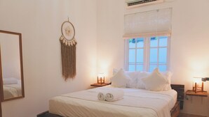 A bedroom with a bed, bedside lamps, a wall hanging, and a window. - Villa The White House Seminyak (Legian)