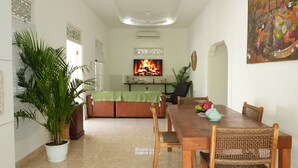 A dining area with a wooden table and chairs, a sofa, and a television displaying a fire. - Villa The White House Seminyak (Legian)