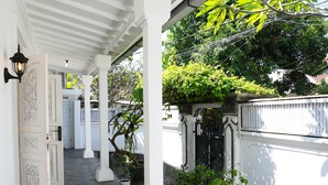A covered walkway with white columns, potted plants, and a gated entrance. - Villa The White House Seminyak (Legian)