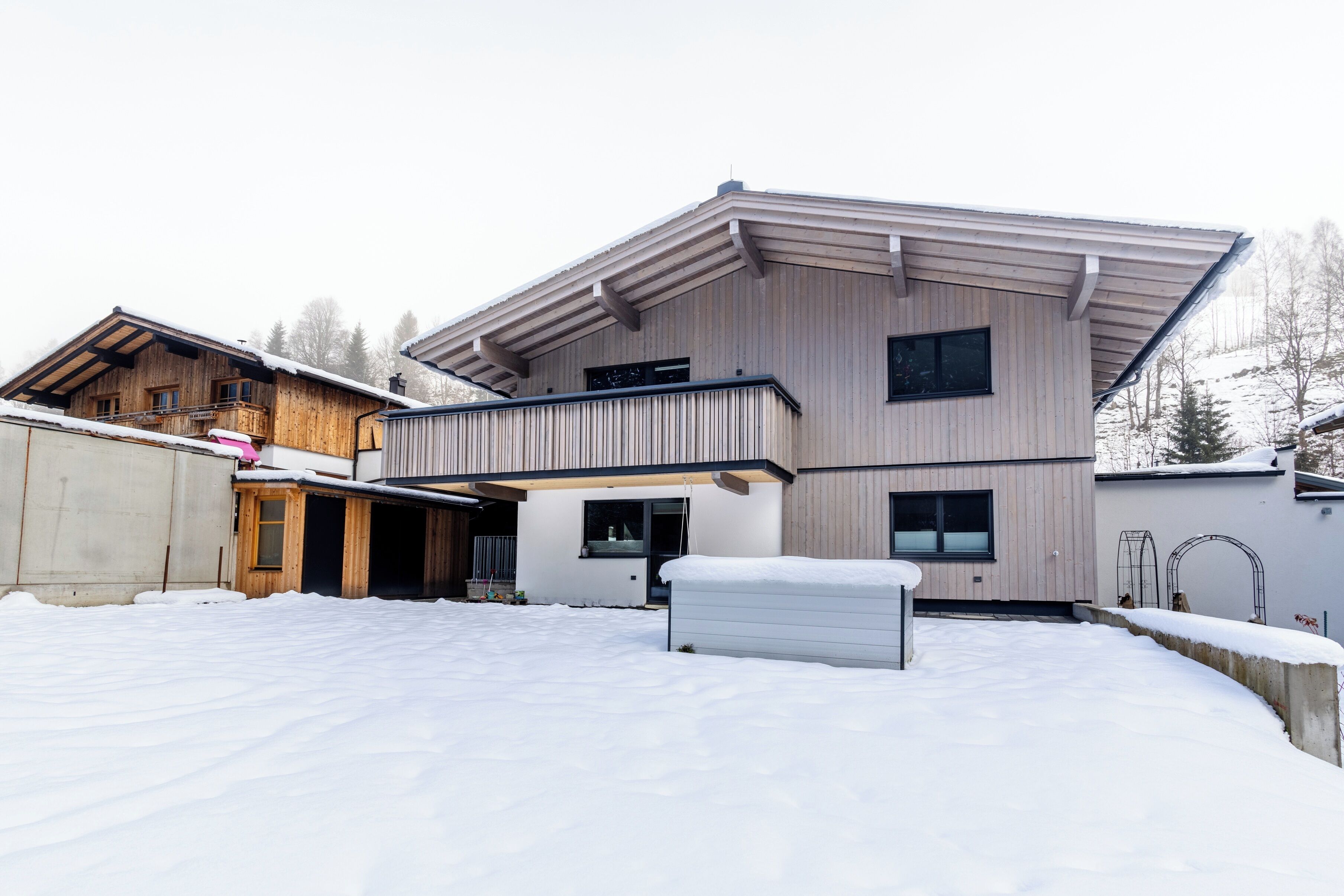 A modern multi-story building with a sloped roof, wooden exterior, and a snow-covered ground.