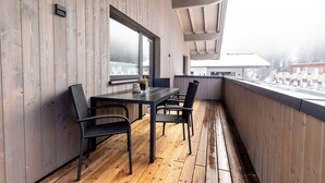 A wooden deck with a table and chairs, a window, and a view of buildings in the distance. - Appartement Hoamatgfüh (Saalbach)