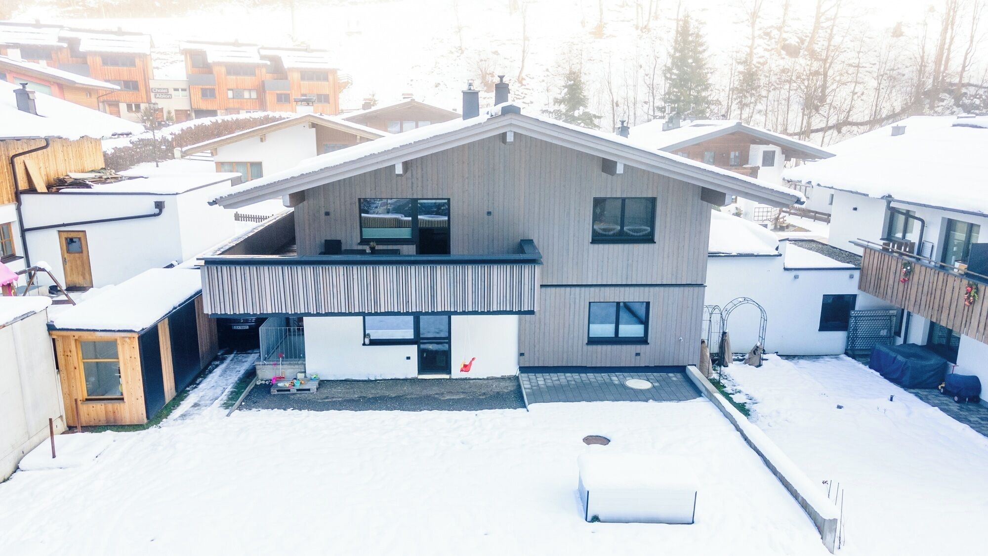 A modern two-story house with a sloped roof, a balcony, and a small front yard covered in snow.