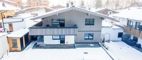 A modern two-story house with a sloped roof, a balcony, and a small front yard covered in snow.