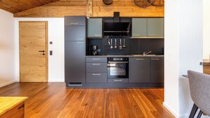 A modern kitchen with dark cabinets, a stainless steel range hood, and a wooden ceiling. - Appartement Hoamatgfüh (Saalbach)