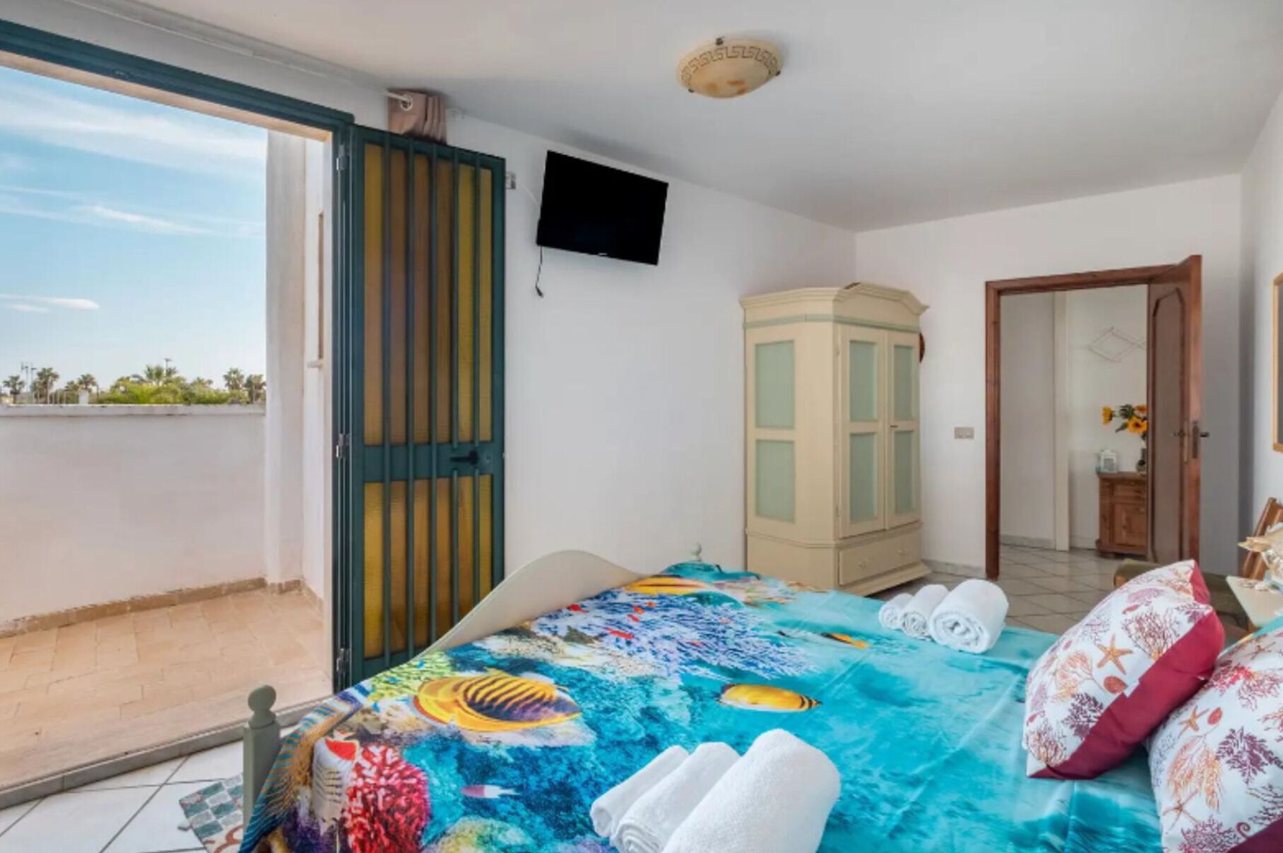Een slaapkamer met een bed, een kledingkast, een televisie en een balkon.