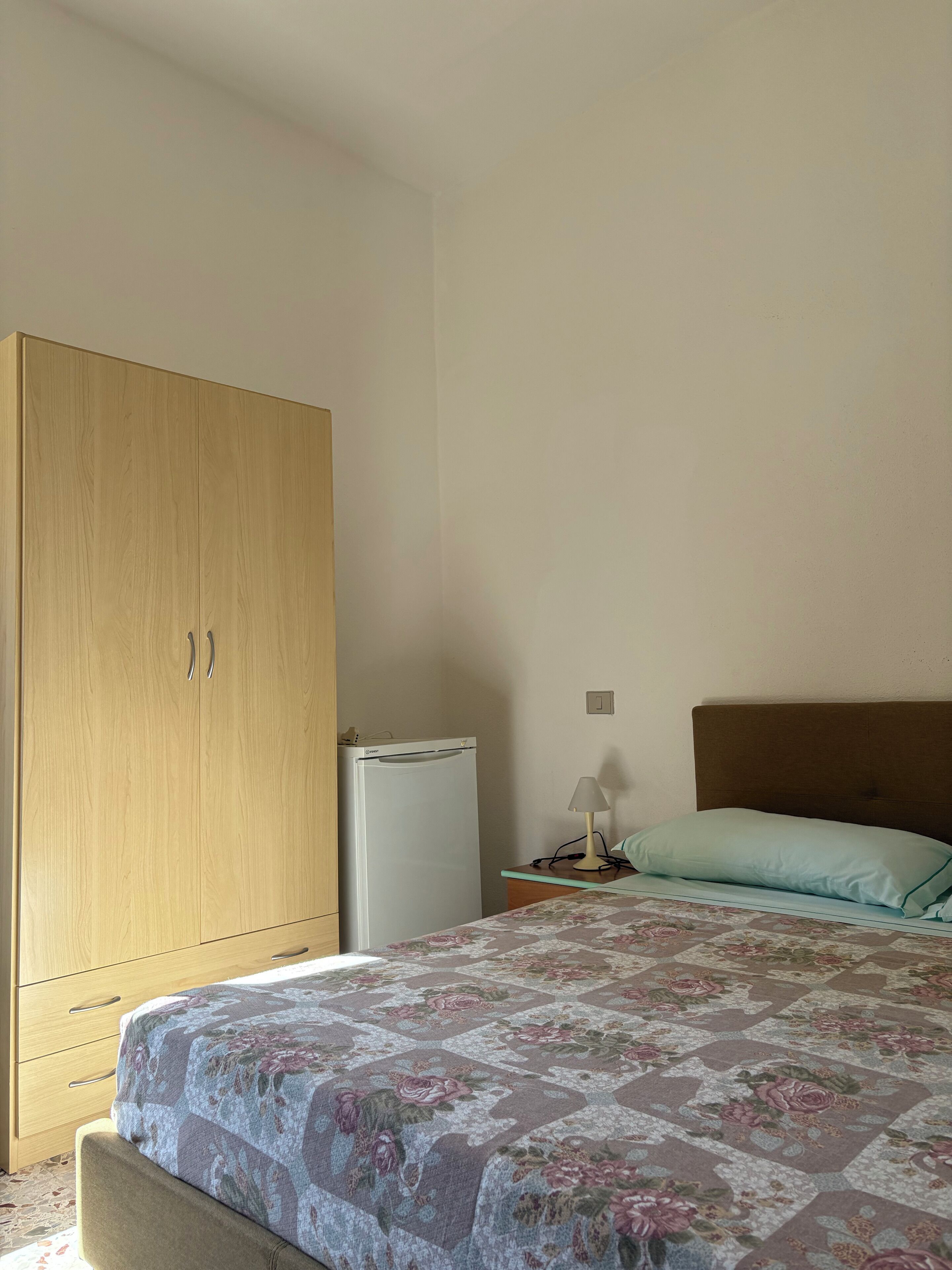 Une chambre à coucher comprenant un lit, une armoire, une petite table avec une lampe et un réfrigérateur.