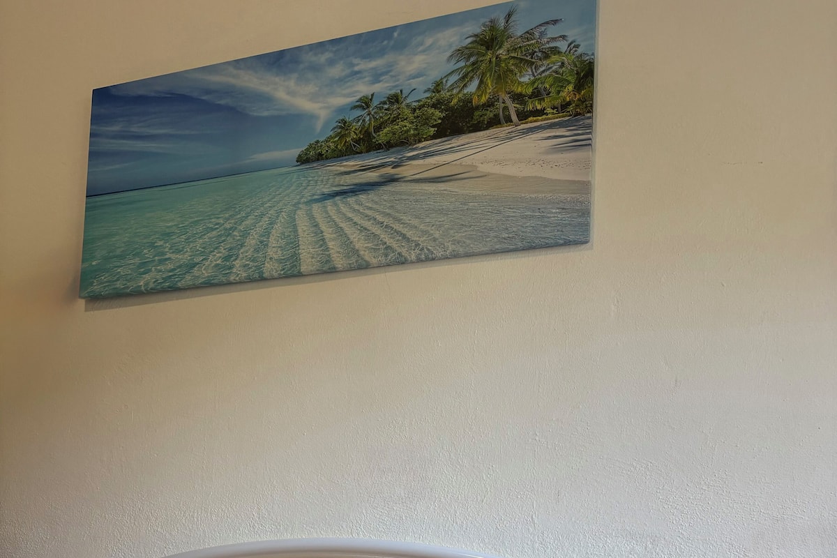 A bed with a colorful quilt, a white metal headboard, and a painting of a beach scene above it.