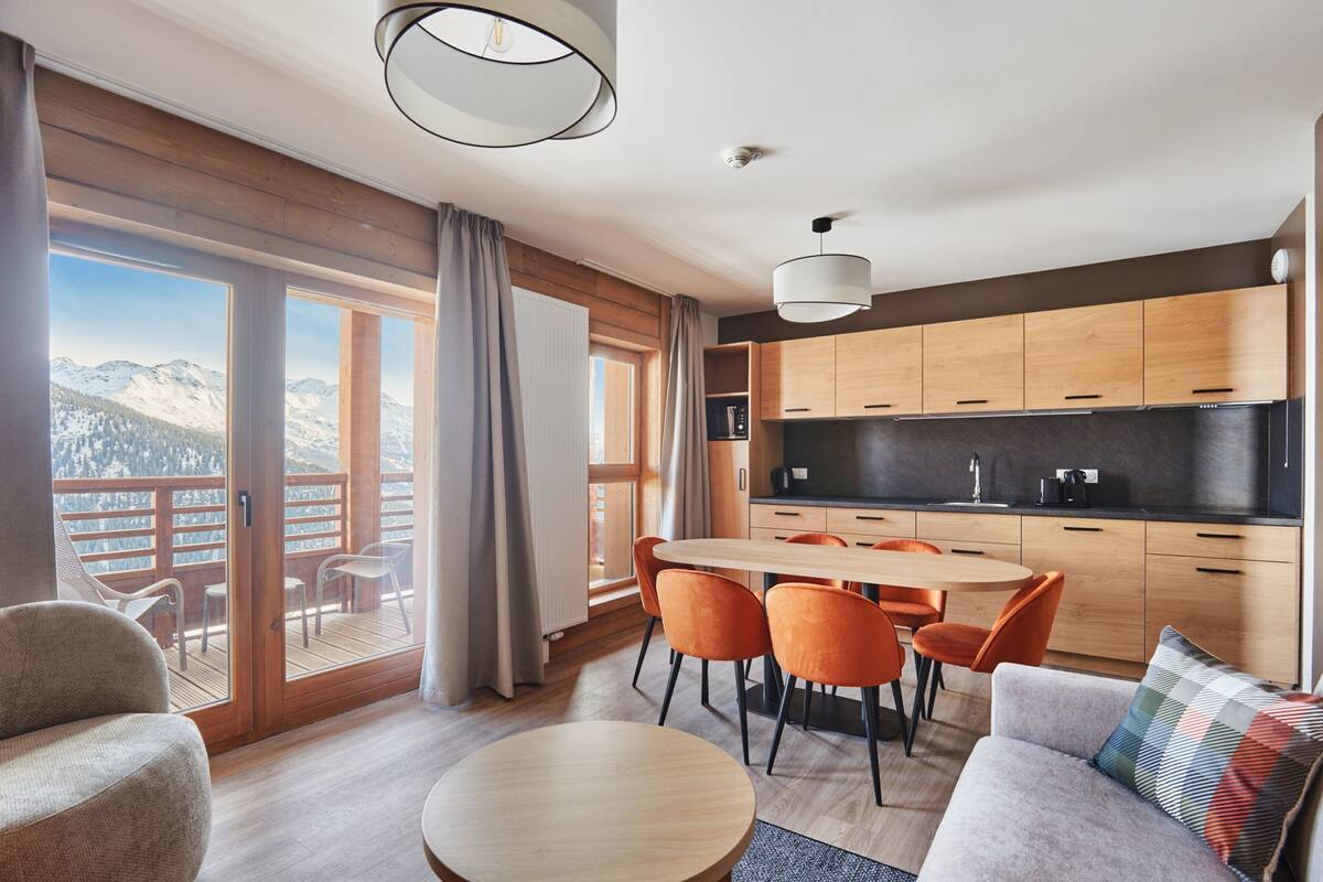 Eine moderne Küche mit Holzschränken, einer schwarzen Arbeitsplatte und einem Essbereich mit orangefarbenen Stühlen.