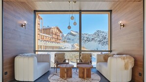 A modern interior with a large window offering a mountain view, two sofas, a coffee table, and wall-mounted lighting. - Résidence Odalys L'Ecrin Blanc (La Rosiere)