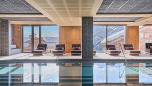A modern indoor pool area with lounge chairs and a view of mountains through large windows. - Résidence Odalys L'Ecrin Blanc (La Rosiere)