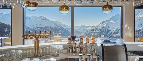 Zona de bar con vista a la montaña, grifo de cerveza y diferentes botellas y vasos.