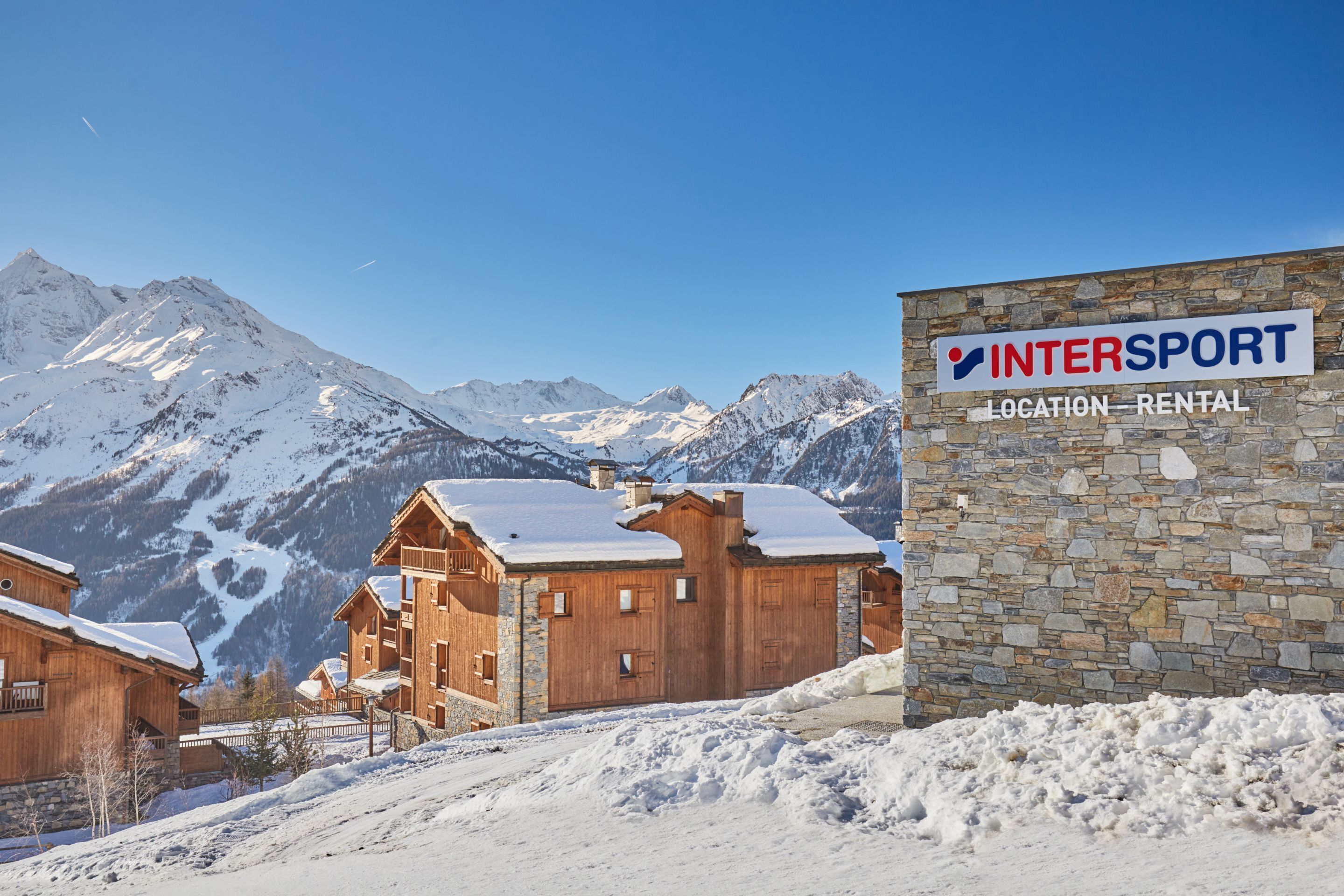A wooden lodge with a stone wall and a sign for InterSport location rental.